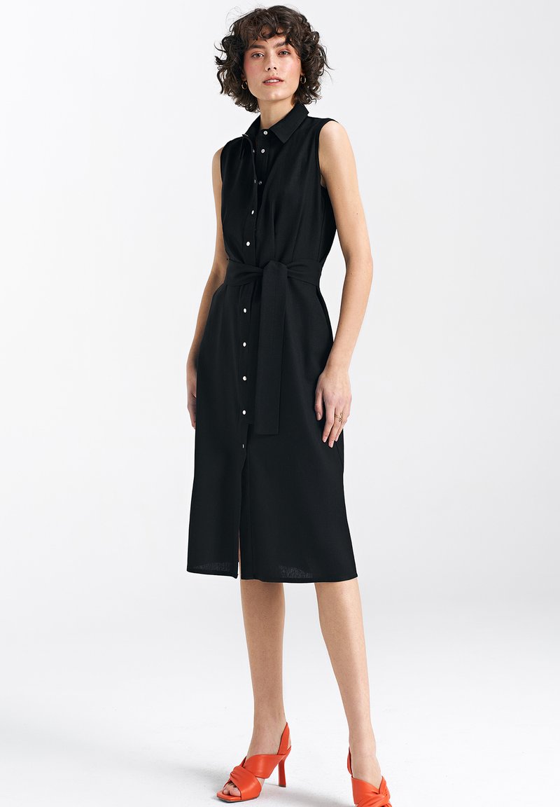 Czarna, bezrękawnikowa sukienka midi z zapięciem na guziki z przodu, z wiązaniem w talii i prostym krojem. Posiada gładką teksturę.