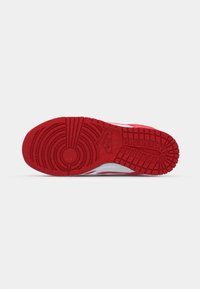 Piros gumitalpú sneaker, kör alakú mintázattal, mély barázdákkal és texturált felülettel. A Nike logo a talp oldalára van lenyomva.