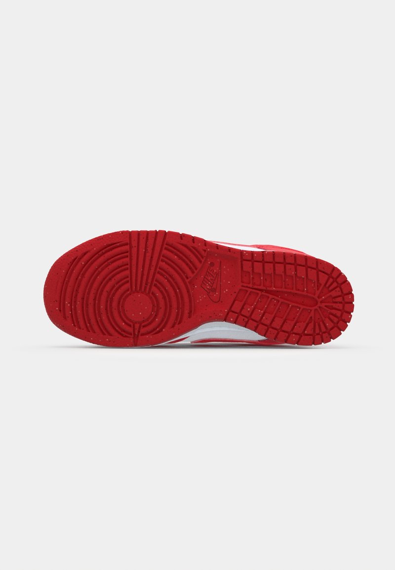 Semelle de sneaker en caoutchouc rouge, présentant un motif circulaire, de profondes rainures et une surface texturée. Le logo Nike est embossé sur le côté.