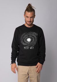 Zwarte sweatshirt met een Melkweg grafiek in het wit, featuring een sterrenachtige spiraalontwerp met een centraal wit gebied en tekst eronder.