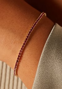 Goldarmband mit einer Reihe kleiner, runder, rosa Edelsteine. Das Armband ist dünn und zierlich und liegt auf einem strukturierten Handgelenk.