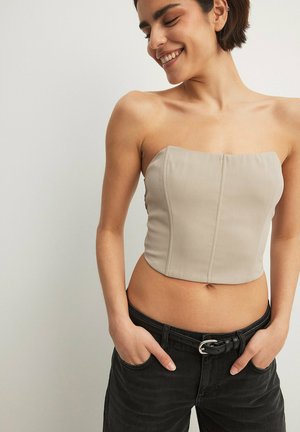 Beež rihmata tops struktuurse bodice'iga, millel on vertikaalsed õmblused ja lühike disain, kombineeritud mustade teksade ja vööga.