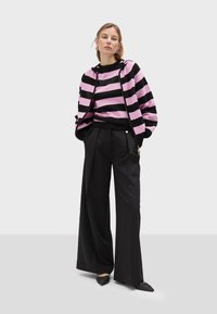 Felpa con zip a strisce rosa e nera, dal taglio rilassato, abbinata a pantaloni neri a vita alta e a gamba larga, completati da scarpe flat nere.