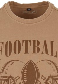 Beige bomulds t-shirt med rund halsudskæring, med en brun "FOOTBALL" print og grafik af en fodbold og hjelme. Størrelsesmærkat inkluderet.