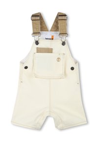 Salopette courte en velours côtelé beige clair avec bretelles ajustables, poche avant et logo Timberland. Le tissu est d'une couleur crème claire avec des détails de couture.