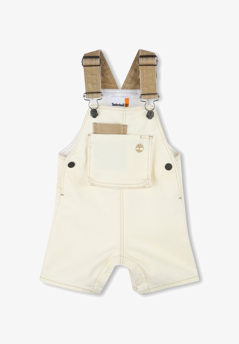 Salopette corta in corduroy color tan con bretelle regolabili, tasca anteriore e logo Timberland. Il tessuto è di un colore crema chiaro con dettagli di cucitura.