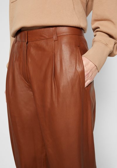 Calças de couro castanho com uma textura suave, apresentando bolsos laterais e um ajuste tailorizado. A cintura é plana com um brilho subtil.