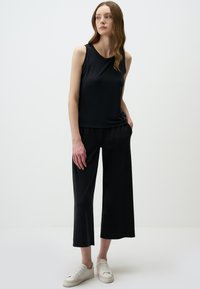 Top nero senza maniche con scollatura rotonda, abbinato a culotte nere ampie. Indossato con sneakers bianche, che mettono in risalto un design minimalista.