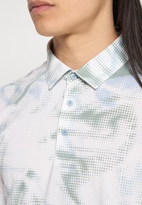 Leichtes Hemd zum Zumachen mit spitzem Kragen, mit einem gepunkteten Muster in Grün- und Blautönen auf weißem Hintergrund.