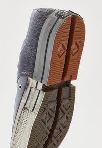 Graue Canvas-Hohe-Sneaker mit strukturierten Details, Gummisohle, orangefarbenen Gummiakzenten und schwarzen Streifen an den Seiten. Chuck Taylor-Label sichtbar.