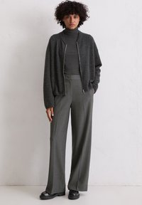 Sivi zip-up kardigan preko tamne rolke, uparen s hlačama visokog struka širokih nogavica u sivoj boji i crnim platformskim cipelama.