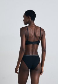 Ensemble de lingerie noire comprenant un soutien-gorge lisse et élégant avec des bretelles réglables, et une culotte taille haute assortie avec un accent subtil à la taille.