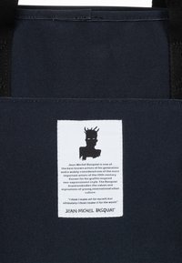 Laukkumalli esittää laivastonsinistä kudottua kanvaslaukkua mustilla kudotuilla hihnoilla. Laukun mukana on valkoinen etiketti, jossa on siluetti ja teksti Jean-Michel Basquiasta.