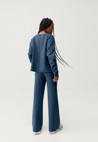 Niebieski, gładki, ponadwymiarowy sweter z opadającymi ramionami oraz szerokie spodnie, oba w dopasowanym kolorze. Widać również trampki.