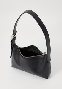 Sac à main en cuir noir avec une forme structurée, un fond plat et une fermeture zippée. Il dispose d'une anse rembourrée et d'un extérieur lisse.
