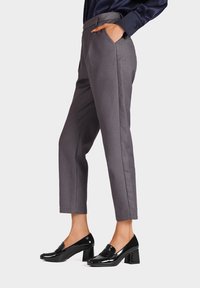 Pantaloni grigi su misura con tasche laterali, dal fit slim e pieghe ben definite. Abbinati a mocassini neri lucidi con tacco.