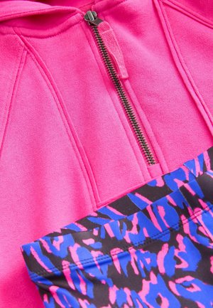 Hvale megna rožnate zip-up kapuce z kapuco in šivanim podrobnostim. Ujemajoče se črne in modre legice z vzorcem, ki vsebuje drzen živalski tisk.