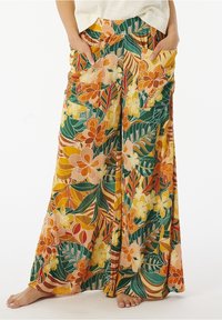 Pantalons larges à fleurs en orange, jaune et vert, présentant un mélange de grandes fleurs et de motifs feuillus. Comprend des poches sur les côtés et un tissu texturé.