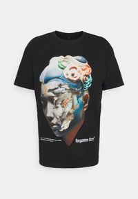 Sort bomulds T-shirt med et grafisk motiv af et stiliseret ansigt med farverige accenter, teksturerede hårelementer og tekst, der siger "glemte ansigtstræk."