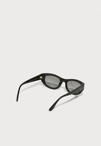 Black cat-eye sunglasses with a glossy finish, gray lenses, gold hardware accents, and a slightly curved shape. Features logo on the side.