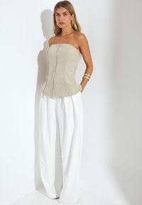 Beige strapless top with vertical seams and slight peplum. Paired with loose white pleated trousers. Smooth fabric texture. Gold bracelet accessory.