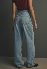 Ljusblå högmidjade jeans med vida ben, med två bakfickor och en blekt denimstruktur. Svarta skor syns nedanför.