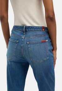 Niebieskie dżinsy o prostym kroju, z talią o średnim wzroście, pięcioma kieszeniami i subtelnymi przeszyciami z tyłu.