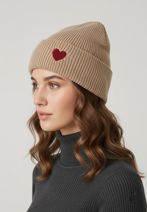 Beige ribbed knit beanie with a red heart patch. The hat has a slightly pointed top and is worn with a gray turtleneck.