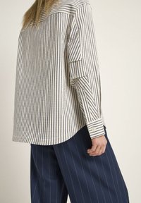 Striped button-up shirt in cream and navy, featuring a relaxed fit, long sleeves with a two-button cuff, and a curved hemline.