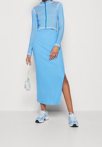 Light blue athletic outfit featuring a fitted, cropped, ribbed long-sleeve top and a flowing maxi skirt with a side slit, paired with sneakers.