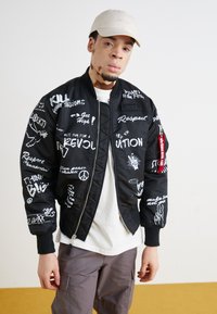 Black bomber jacket with white graphic text and designs, featuring a front zip closure, ribbed cuffs, and a red tag on the zipper.