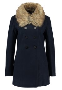 Manteau croisé bleu marine avec six boutons et un grand col en fourrure beige duveteuse.