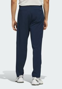 Marineblauwe golfbroek met een gestructureerd oppervlak, voorzien van twee achterzakken en een verstelbare tailleband, gecombineerd met witte sportschoenen.