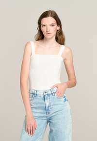 White fitted bodysuit with square neckline and wide straps, paired with light blue high-waisted denim jeans featuring a slight acid wash.