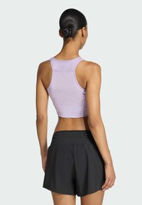 Svetlofialový crop top s pretekárskym strihom, kombinovaný s čiernymi športovými šortkami, vystavujúci hladký materiál a voľný strih.