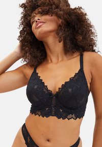 Bralette in pizzo nero con bordi scallop, motivi floreali, spalline regolabili e chiusura a gancio al centro anteriore.