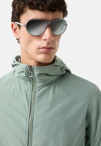 Light green, hooded jacket with a zip closure, made of smooth material, paired with oversized, gray gradient sunglasses with transparent frames.