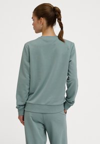 Ljusgrön sweatshirt i mjukt material med rund halsringning, ribbade ärmslut och fåll, med en enkel design utan mönster eller detaljer.