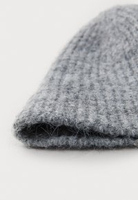 Grijze gebreide muts met een geribbelde structuur, gemaakt van zachte wol, omgeslagen bij de manchet, met losse, pluizige vezels voor extra warmte.