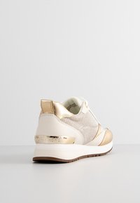 Baskets blanches et dorées pour femmes avec côtés en mesh, languette de talon dorée métallique et accents, semelle blanche et semelle extérieure marron texturée.