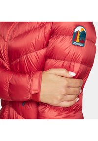 Czerwona kurtka puchowa z pikowaniem w kształcie zygzaka, wykonana z błyszczącego materiału. Posiada naszywkę z logo na rękawie oraz zapięcie na rzep przy mankietach.