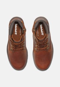 Botas de tobillo de cuero marrón con punta redonda, ojales de metal dorado, cordones bicolor, cuello acolchado y marca Timberland en las plantillas.