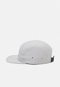 Gray cap with a flat brim, made of canvas fabric. Features ventilation eyelets and a black adjustable strap at the back.