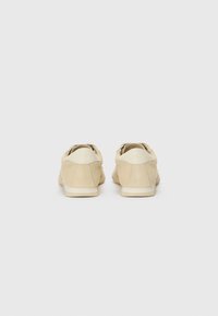 Beige suede shoes with a low-top design, smooth texture, and a white rubber sole. Features a subtle logo on the heel and minimal stitching.