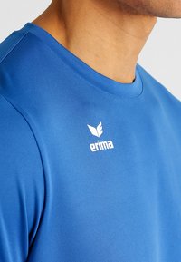 Blauwe sport t-shirt gemaakt van gladde stof. Heeft een ronde hals en een wit logo op de linker schouder. Eenvoudig ontwerp.