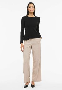 Czarna prążkowana bluzka z długim rękawem i rozkloszowaną talią, zestawiona z beżowymi spodniami o szerokich nogawkach. Buty są czarne, z noskiem w szpic i obcasem typu szpilka.