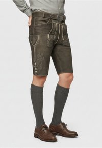 Tmavě hnědé lederhosen s dekorační vý�šivkou, kontrastním světlým šitím a knoflíkovými detaily, doplněné šedými ponožkami do délky kolen a hnědými botami.