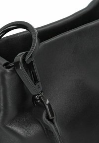 Czarna skórzana torba z połyskującym czarnym okuciem. Powierzchnia ma gładką teksturę, podkreśloną czystymi, nowoczesnymi liniami.