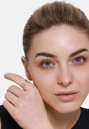 Silberner, verdrehter Ring an einer Hand mit neutralem Hautton. Der Ring hat zwei sich kreuzende Stränge mit einer polierten Oberfläche.