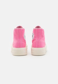 Pár růžových vysokých tenisek Converse s bílými podrážkami pohledem zezadu na bílém pozadí.